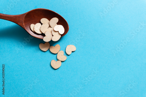 A lot of tiny wooden hearts in a wooden spoon on a blue background.