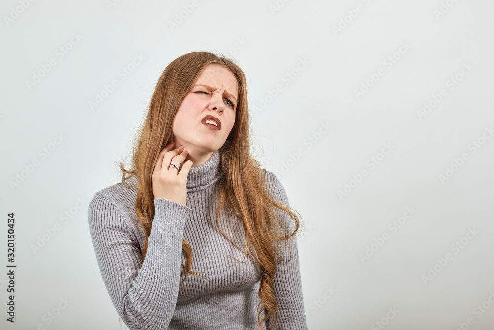 A young beautiful woman with red hair in a gray sweater has a sore neck and holds her hand to her cheek A young beautiful woman with red hair in a gray sweater has a sore neck and holds her hand to her cheek