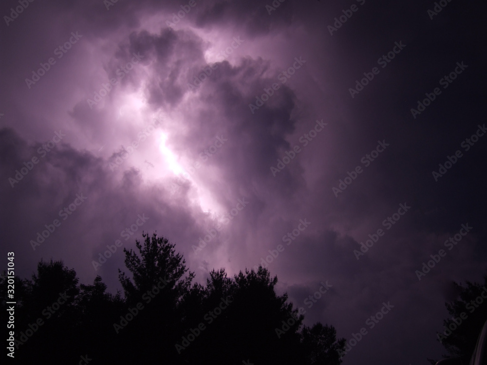 cloud to cloud lightning against purple sky at night with pine trees cloud to cloud lightning against purple sky at night with pine trees