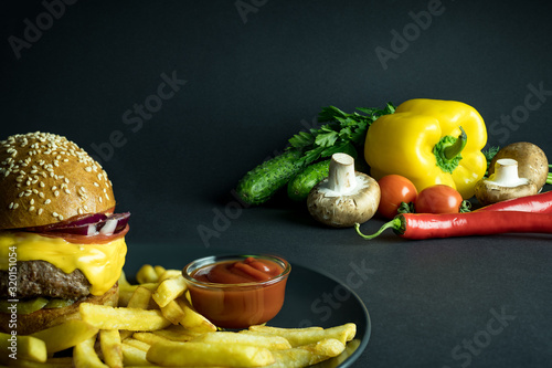 Fototapeta Naklejka Na Ścianę i Meble -  Hamburger with french fries and ketchup near organic vegetables on black background