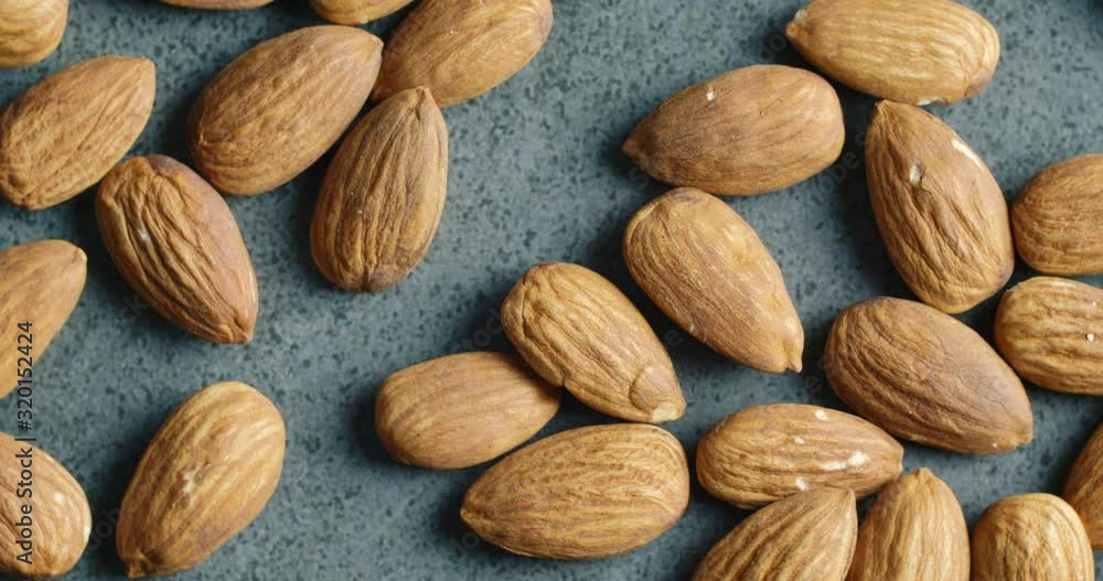 Many fresh almonds nuts rotating on dark kitchen surface. Close up macro shot of almond. 