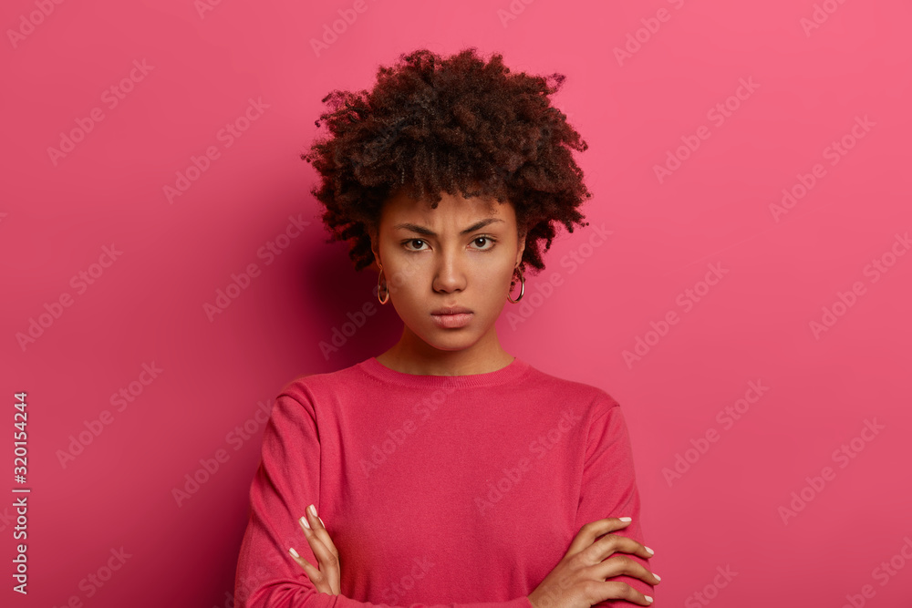 Bossy displeased curly woman holds hands crossed, looks angrily at ...