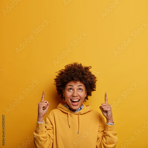 Foto Glad dark skinned female introduces blank space above for your advertisement, su