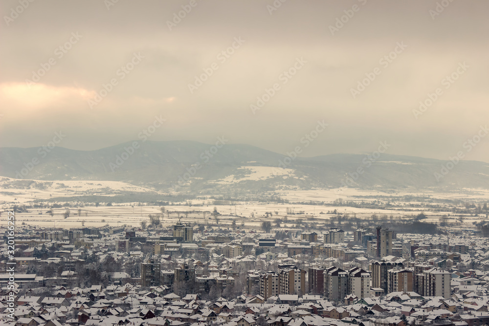 Beautiful dreamy snow covered winter Pirot cityscape and murky, cloudy sky before sunset