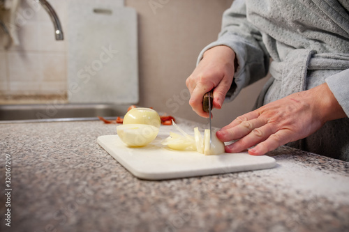 Women's hands cuting white onions with a knife on a cutting Board in the kitchen. Non-personalized. Healthy food, vegetarian products.