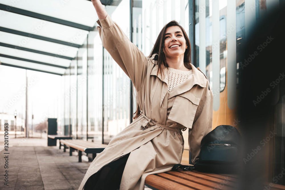 Obraz premium Positive young woman sitting at a public transport stop and waving