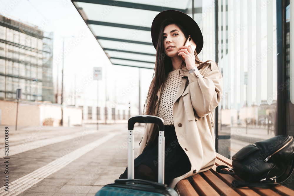 Fototapeta premium Stylish girl dressed in a coat and hat talking on the phone when waiting for public transport
