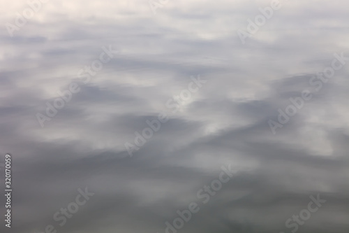 Abstract background - Reflection of cloudy, neutral sky in the water surface patterns with dark and shiny patches © Nikola