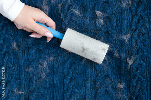 Woman hand using a sticky roller to clean fabrics - woolen knitted sweater from dust, hair, lint and animal fluff, top view, close up. photo