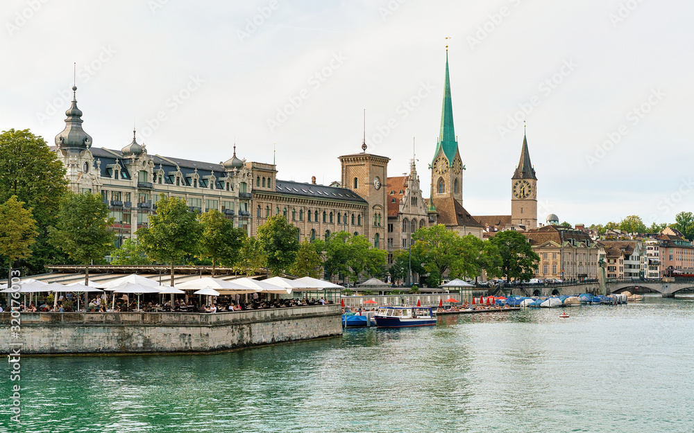 Zurich, Switzerland - September 2, 2016: Restaurant terrace at Limmat River quay and Saint Peter Church and Fraumunster Church in the city center of Zurich, Switzerland.