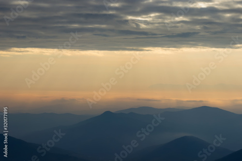 Soft, colorful view of distant mountain layers in Bulgaria from Old mountain in Serbia, lighten by morning sun rays under dramatic, vibrant sunrise sky © Nikola