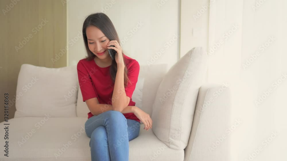 An attractive Asian woman sits on a couch while talking on her smartphone. An attractive Asian woman sits on a couch while talking on her smartphone.