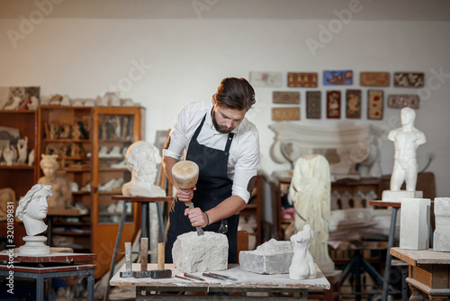 Fototapeta Stone carver works with wooden hammer and chisel at limestone.