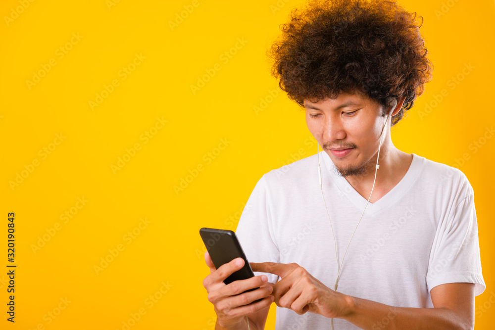 Happy asian handsome man with curly hair he smiling enjoying listening to music on earphones using a mobile smartphone