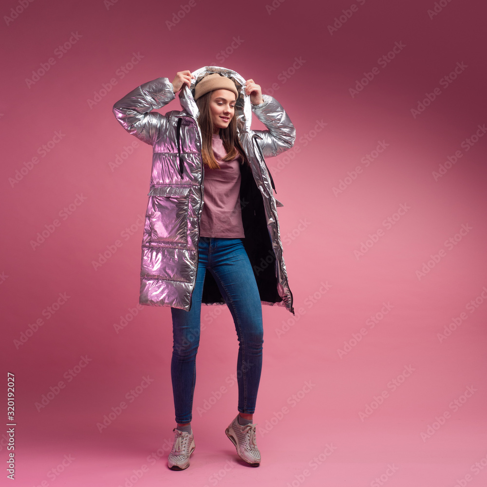 Φωτογραφία fashionable and modern young woman in a puffy light down jacket throws a hood over her head