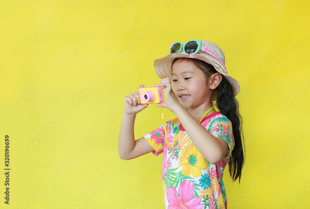 Little girl taking photo by toy camera. Child tourists in floral pattern summer dress and hat with sunglasses isolated over yellow background. Little girl taking photo by toy camera. Child tourists in floral pattern summer dress and hat with sunglasses isolated over yellow background.