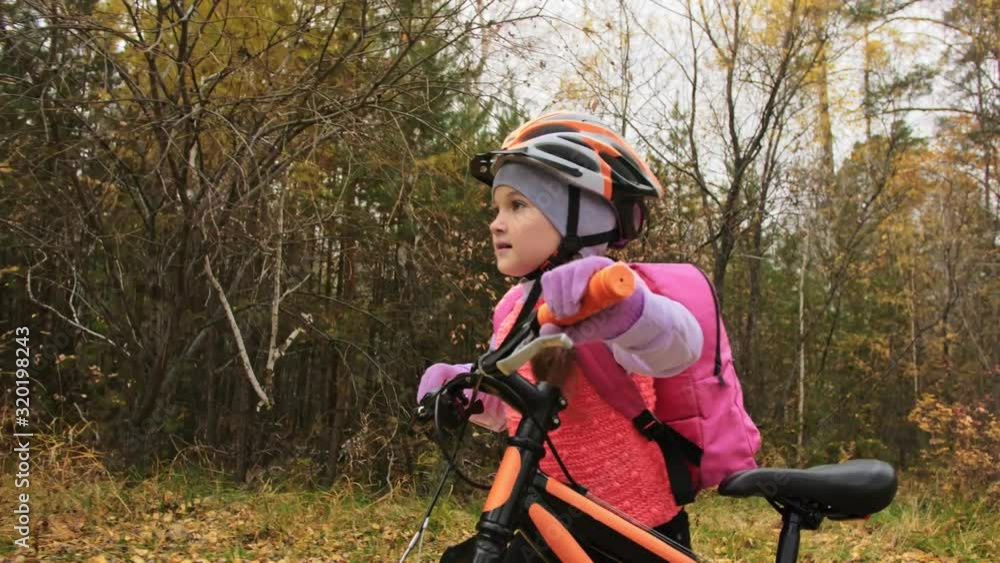 One caucasian children walk with bike in autumn park. Little girl walking black orange cycle in forest. Kid goes do bicycle sports. Biker motion ride with backpack and helmet. Mountain bike hardtail. One caucasian children walk with bike in autumn park. Little girl walking black orange cycle in forest. Kid goes do bicycle sports. Biker motion ride with backpack and helmet. Mountain bike hardtail.