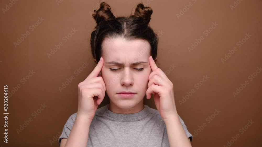 Frustrated woman holding hands on forehead being depressed regretting what she done having headache, wears grey t-shirt, stands over brown background. Negative human emotions and feelings concept Frustrated woman holding hands on forehead being depressed regretting what she done having headache, wears grey t-shirt, stands over brown background. Negative human emotions and feelings concept