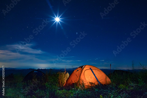 Orange tent lit under the starry sky. Camping tent under the night sky.