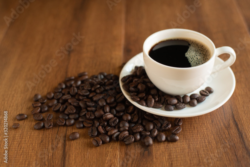 Black coffee in a white cup and coffee beans on a wooden table