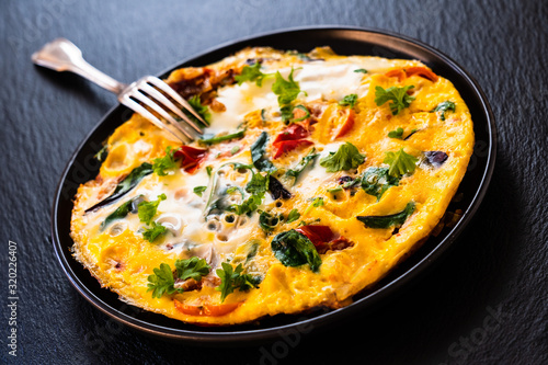 Breakfast - scrambled eggs with vegetables on black stone background