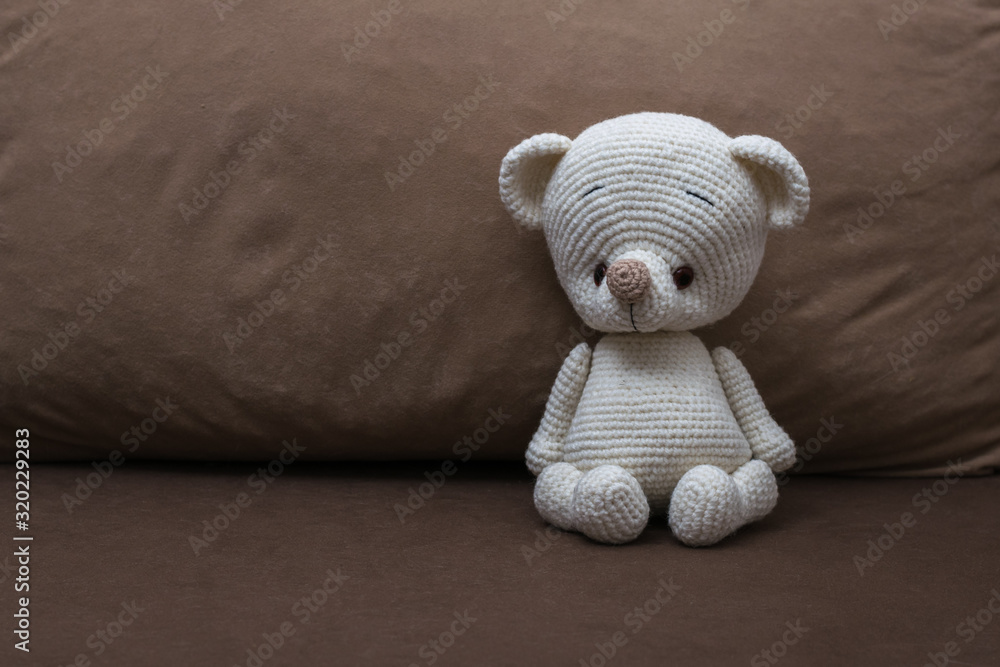 Fototapeta premium A small white knitted bear on a soft sofa.