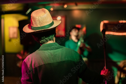 Closeup of male musician holding microphone against artist singing on stage in illuminated auditorium hall at world and spoken word festival