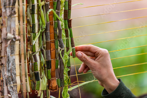 Closeup cropped image of human hand decorating yellow string with green braided leaves and wooden bamboos wampum during world and spoken word festival photo
