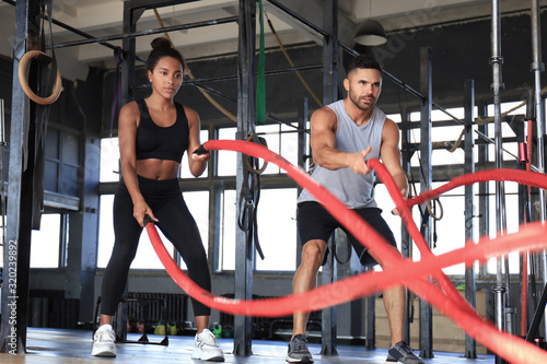 Obraz na plátně Athletic young couple with battle rope doing exercise in functional training fitness gym