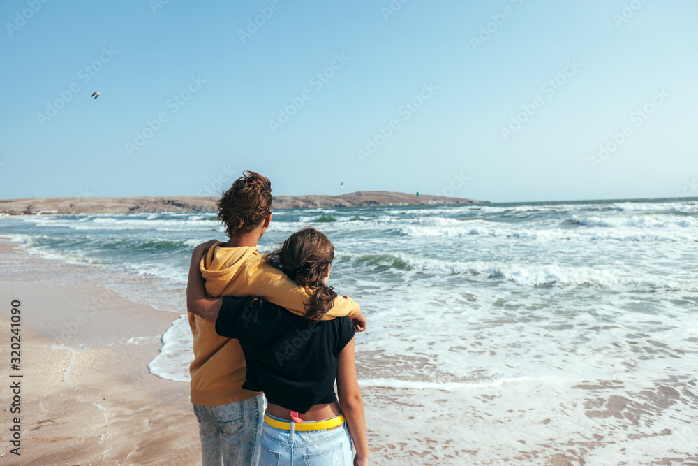 Back view of teenage boy and girl hugging and wathing the sea.