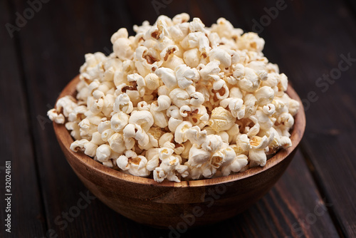 Wooden bowl with salty popcorn on a wooden table. Dark background Selective focus.