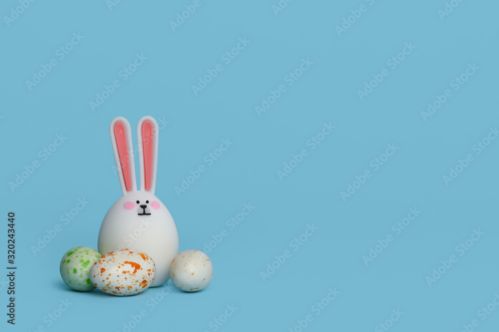  Easter rabbit. White cute toy rabbit with multicolored eggs isolated on blue background. Easter concept. Copy space. 