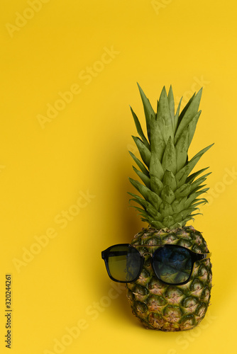  Funny pineapple in summer cool sunglasses on a yellow background. Isolated. Summer vacation concept.
