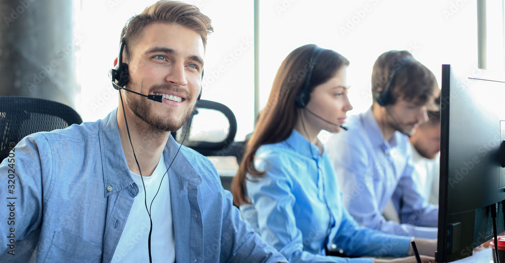 Portrait of call center worker accompanied by his team. Smiling customer support operator at work. - obrazy, fototapety, plakaty 