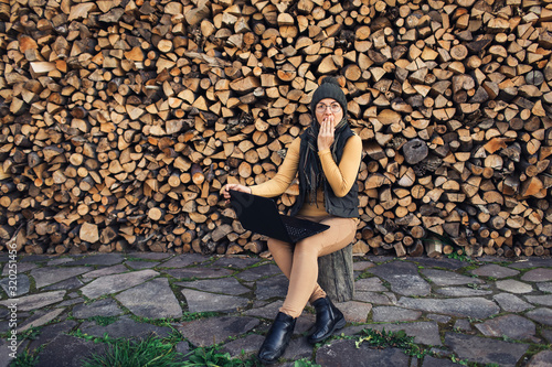 nerd girl in glasses working on laptop on background of wall of firewood. Emotion surprise, shock.
