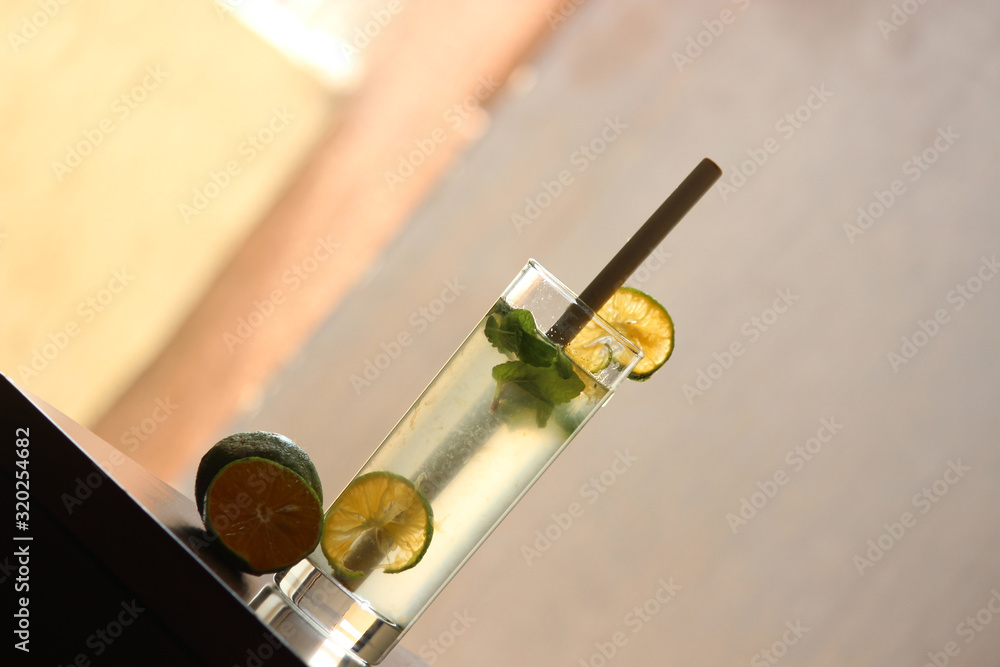 Lemonade soda in Tall glass with bamboo straw with mint leaves and fresh cut lemons in the background