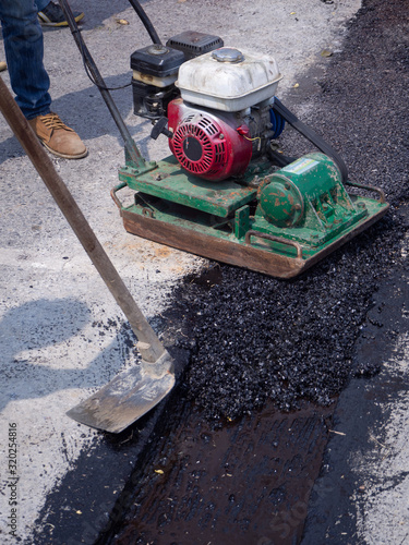 Worker use vibratory plate compactor compacting asphalt at road