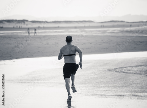 Professional athlete runner man running using heart rate monitor and smart watch training on beach