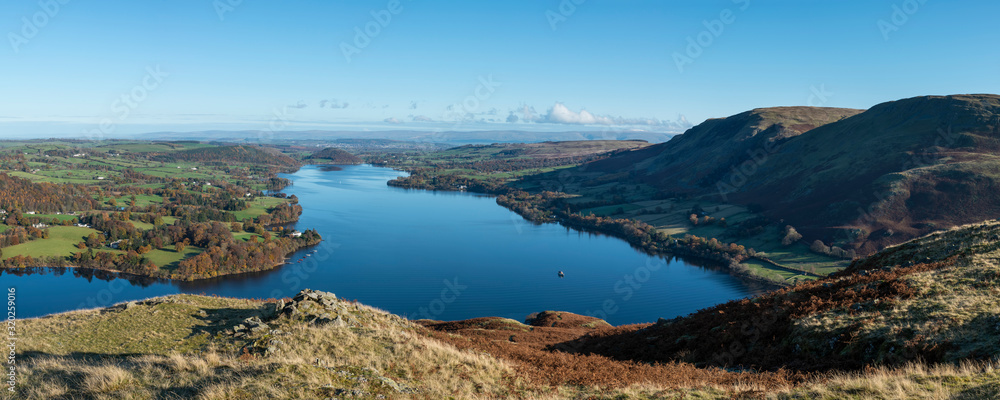 Beautiful Autumn Fall landscape of Ullswater and surrounding mountains and hills viewed from Hallin Fell on a crisp cold morning with majestic sunlgiht on the hillsides