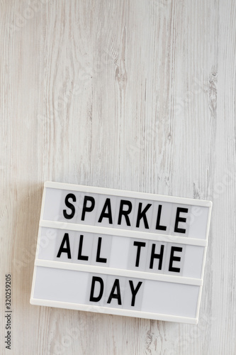 'Sparkle all the day' words on a modern board on a white wooden surface, top view. Overhead, from above, flat lay. Space for text.