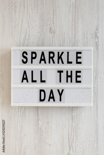'Sparkle all the day' words on a lightbox on a white wooden background, top view. Overhead, from above, flat lay.