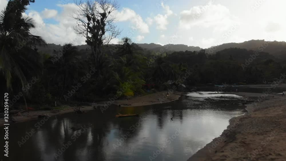 A girl sits at the river edge as it flows into the ocean with a rainforest and sun rays in the background A girl sits at the river edge as it flows into the ocean with a rainforest and sun rays in the background