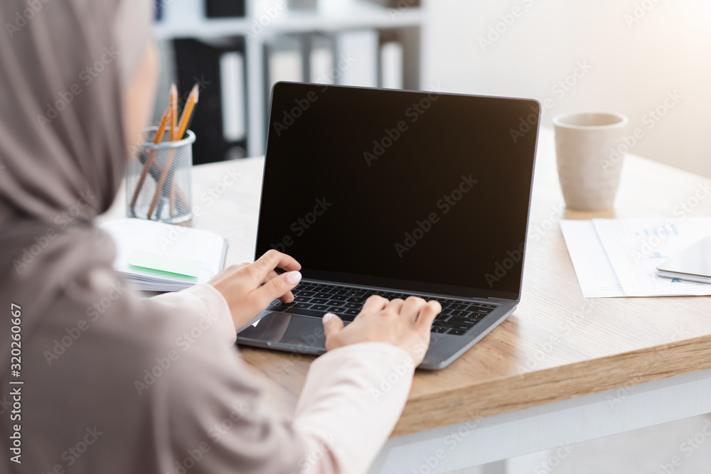 Muslim woman working on laptop with black screen, over shoulder view ...