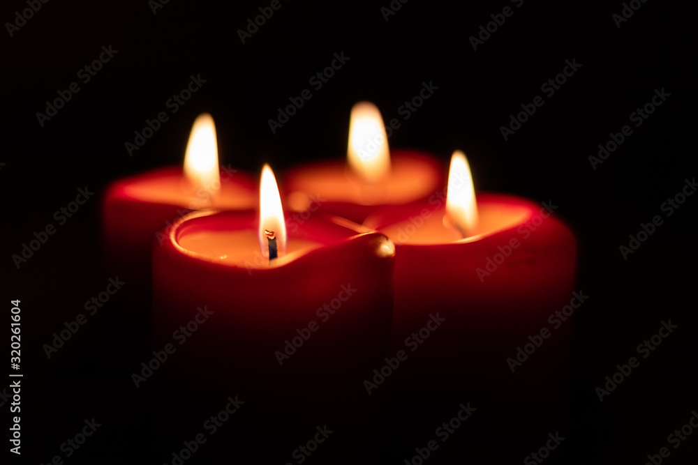 Xmas Christmas season symbol. Four candles symbolize advent weeks. Detail of four red candles burning, isolated with black surrounding. Xmas Christmas season symbol. Four candles symbolize advent weeks. Detail of four red candles burning, isolated with black surrounding.