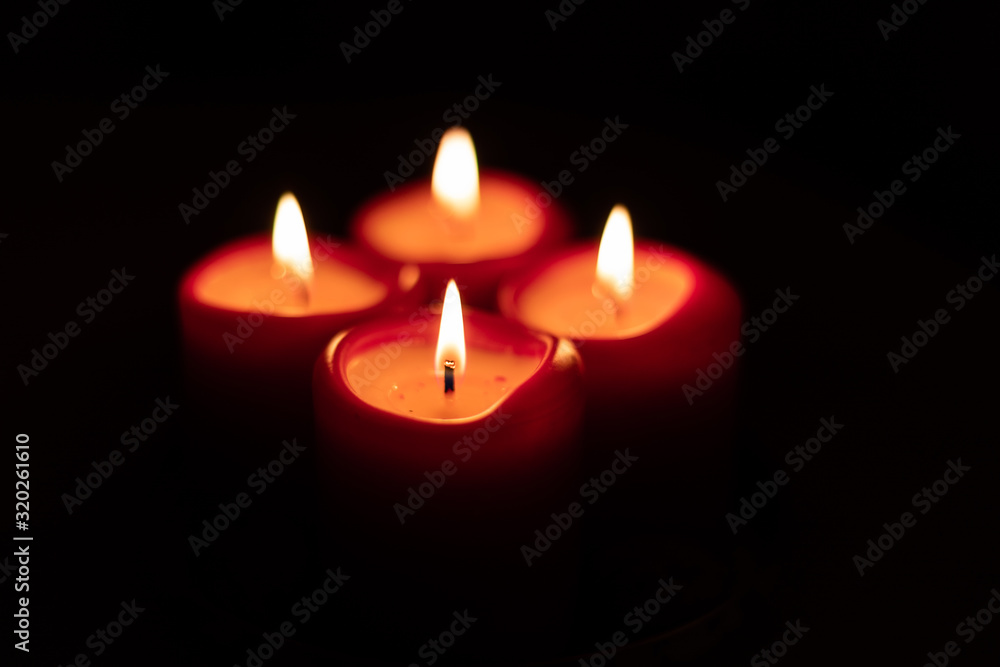 Xmas Christmas season symbol. Four candles symbolize advent weeks. Detail of four red candles burning, isolated with black surrounding.