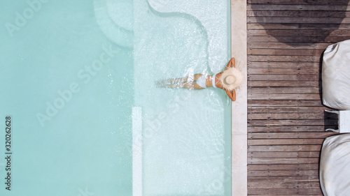 Woman in straw hat relaxing in clear pool water in hot sunny day on Bali villa