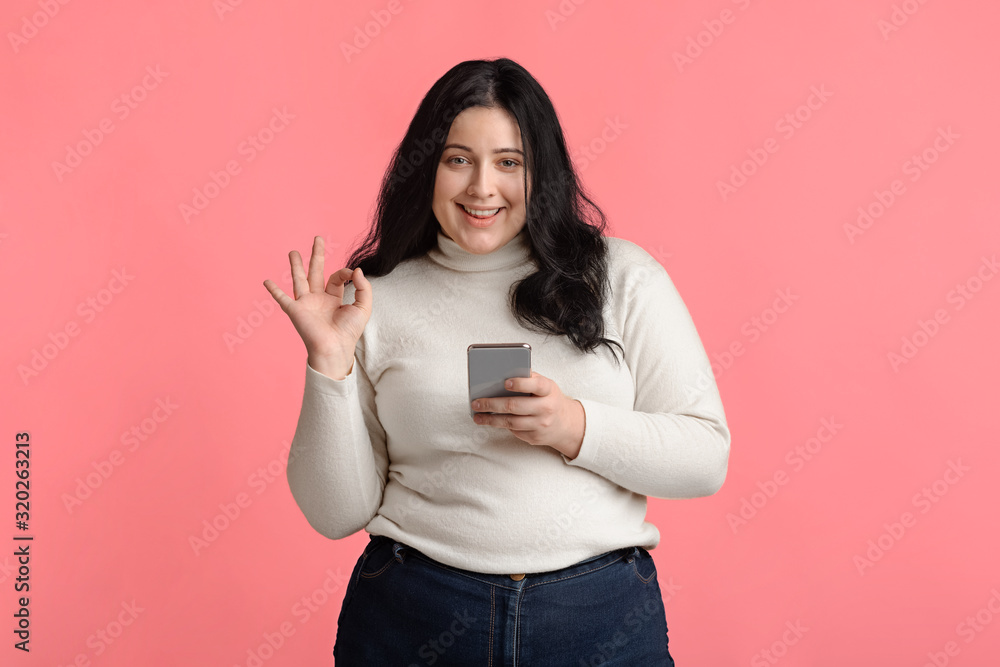 Beautiful Plus Size Model Girl Holding Smartphone And Gesturing Ok Sign Beautiful Plus Size Model Girl Holding Smartphone And Gesturing Ok Sign