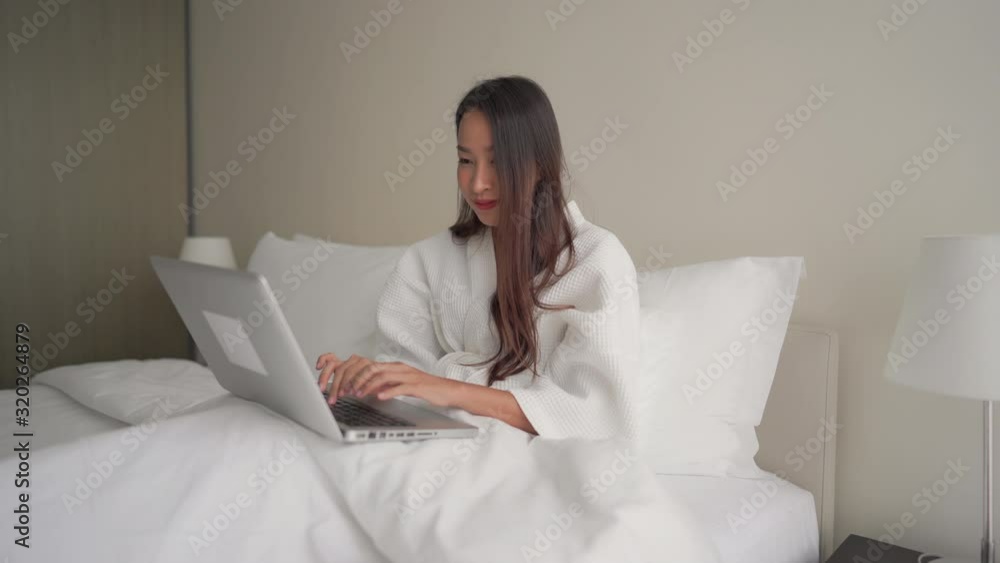 Happy Asian girl working from home with laptop in bed. Interior, static.