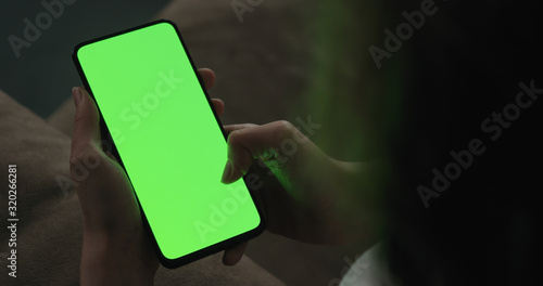 Fotografie Young woman sitting on a couch and using smartphone with green screen