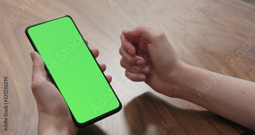 Young woman sitting at a table and using a smartphone with vertical green screen